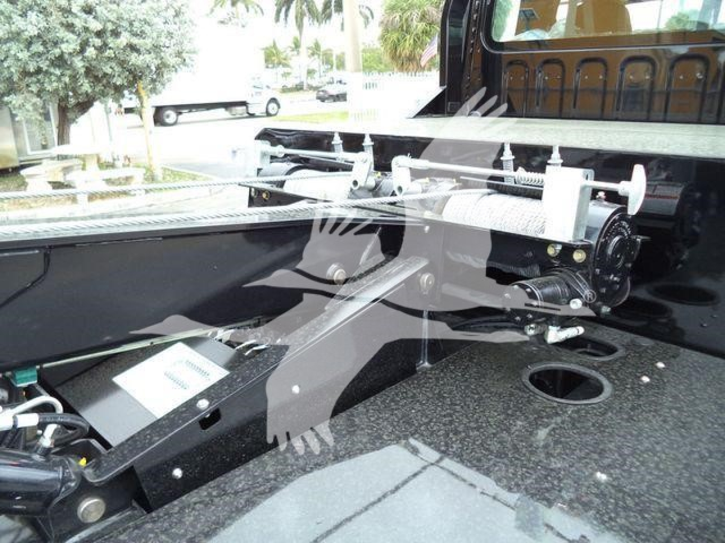 Winch system mounted on truck bed showing winch drum, mounting rails, and control housing with hydraulic line connections.