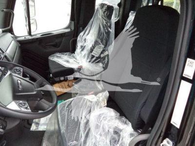 Freightliner M2 106 cab interior showing driver seat with plastic protective cover and steering wheel visible.