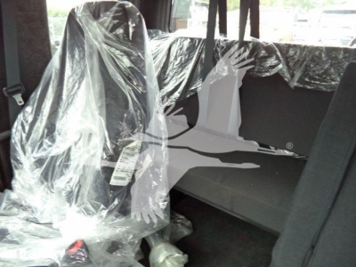 Interior of a Freightliner M2 106 cab with plastic seat covers and a rear jump seat, visible seat belts, and a plastic-wrapped tag hanging from the seat.