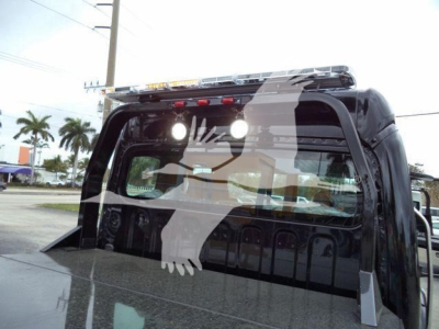 Freightliner M2 106 truck cab rear window and cargo bed with winch equipment visible, roof-mounted emergency lights, and rear cab interior silhouette.