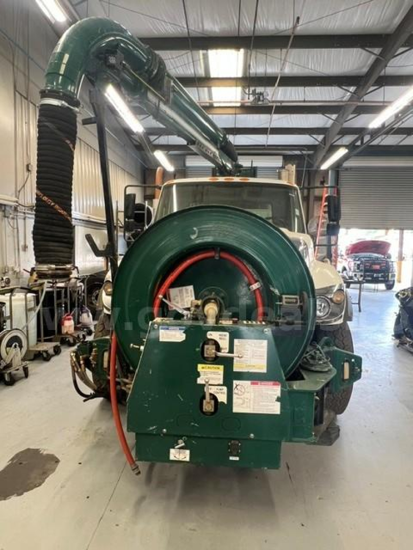 Rear view of a 2019 International 7500 vacuum truck showing a large circular green vacuum blower housing and intake hose, emergency labels, and dashboard controls on back of unit.