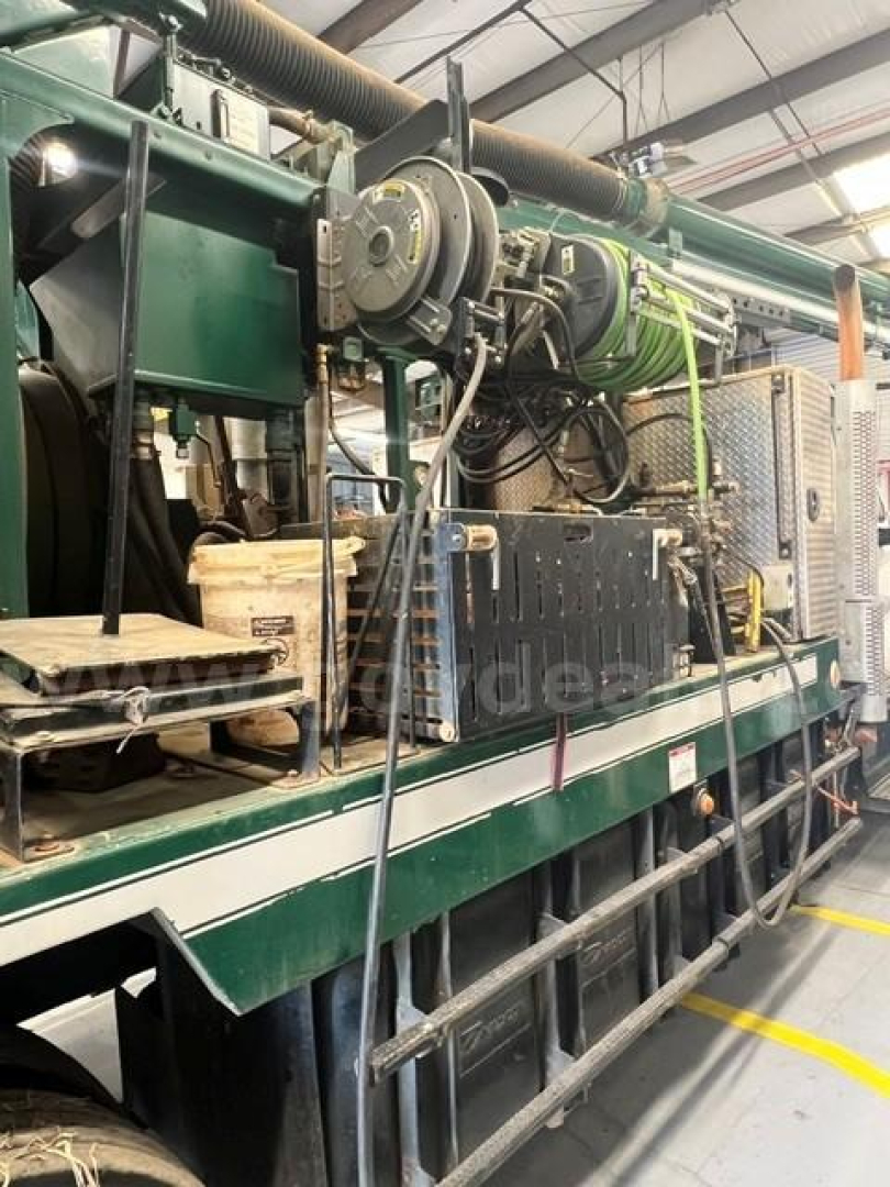 Industrial truck engine bay showing large green machinery with hoses, belts, and control panels. Text on components is not legible.