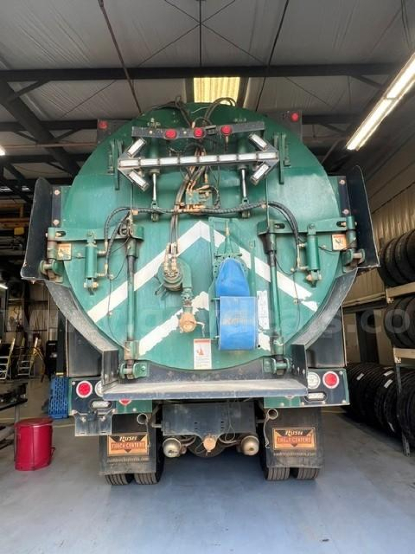 Rear view of a green International 7500 vacuum truck showing hoses and tank fittings