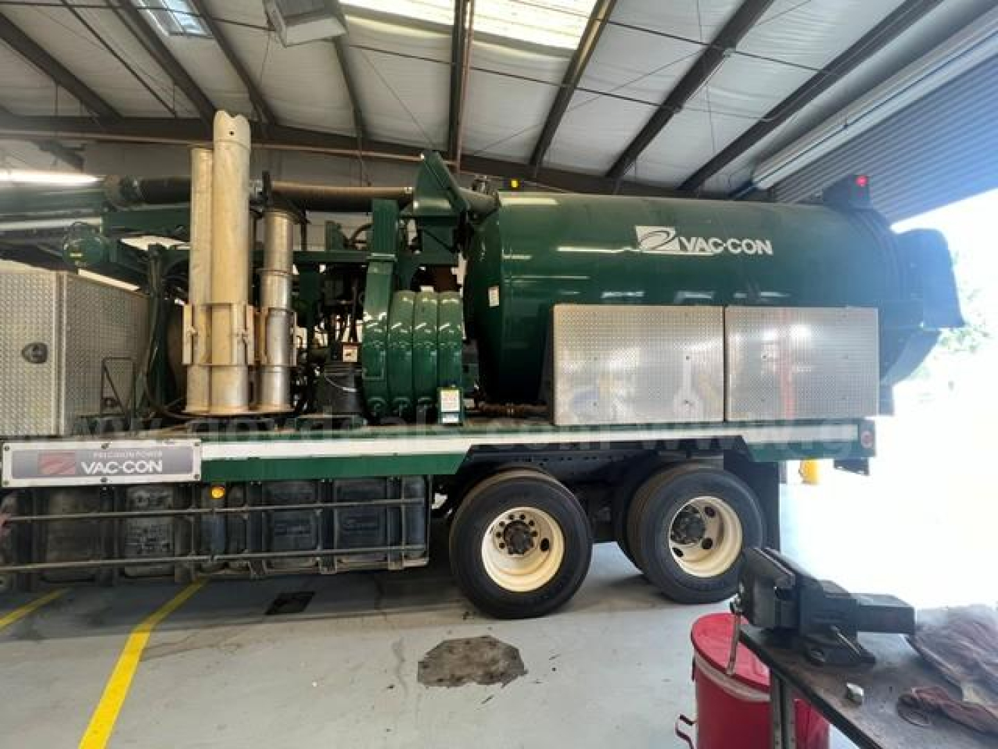 Vac-con unit mounted on truck bed showing green cylindrical vacuum tank and exhaust stack with VAC-CON branding.