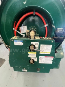 Industrial vacuum truck rear view showing hose reel and control panel with labels and warning decals.