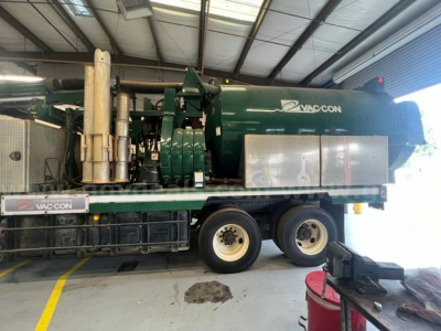 Vac-con unit mounted on truck bed showing green cylindrical vacuum tank and exhaust stack with VAC-CON branding.