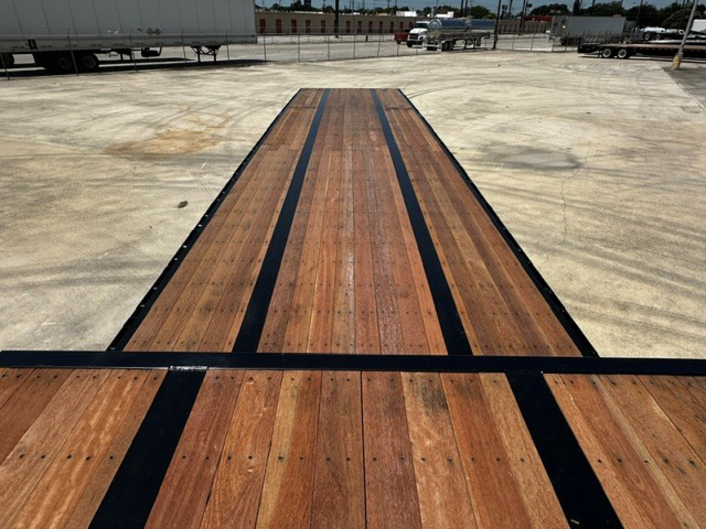 Drop deck trailer bed showing wooden planks with black edge rails and central spine; long perspective toward distance.