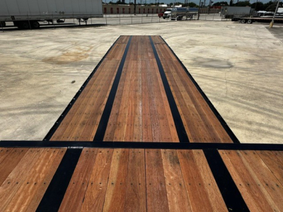 Drop deck trailer bed showing wooden planks with black edge rails and central spine; long perspective toward distance.