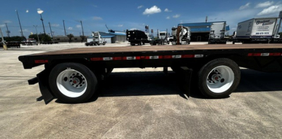 Trailer side view showing 48' drop deck with dual axles and white rims, black deck with red-and-white reflective strips along the length.