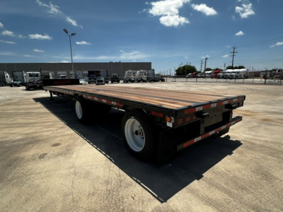 Flatbed trailer with wooden deck and dual rear axles in an open lot, side view showing tail with lights and reflectors.