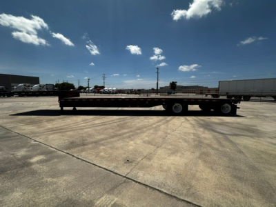 Flatbed trailer in a parking lot, 48 ft drop deck with dual axles and long flat deck.