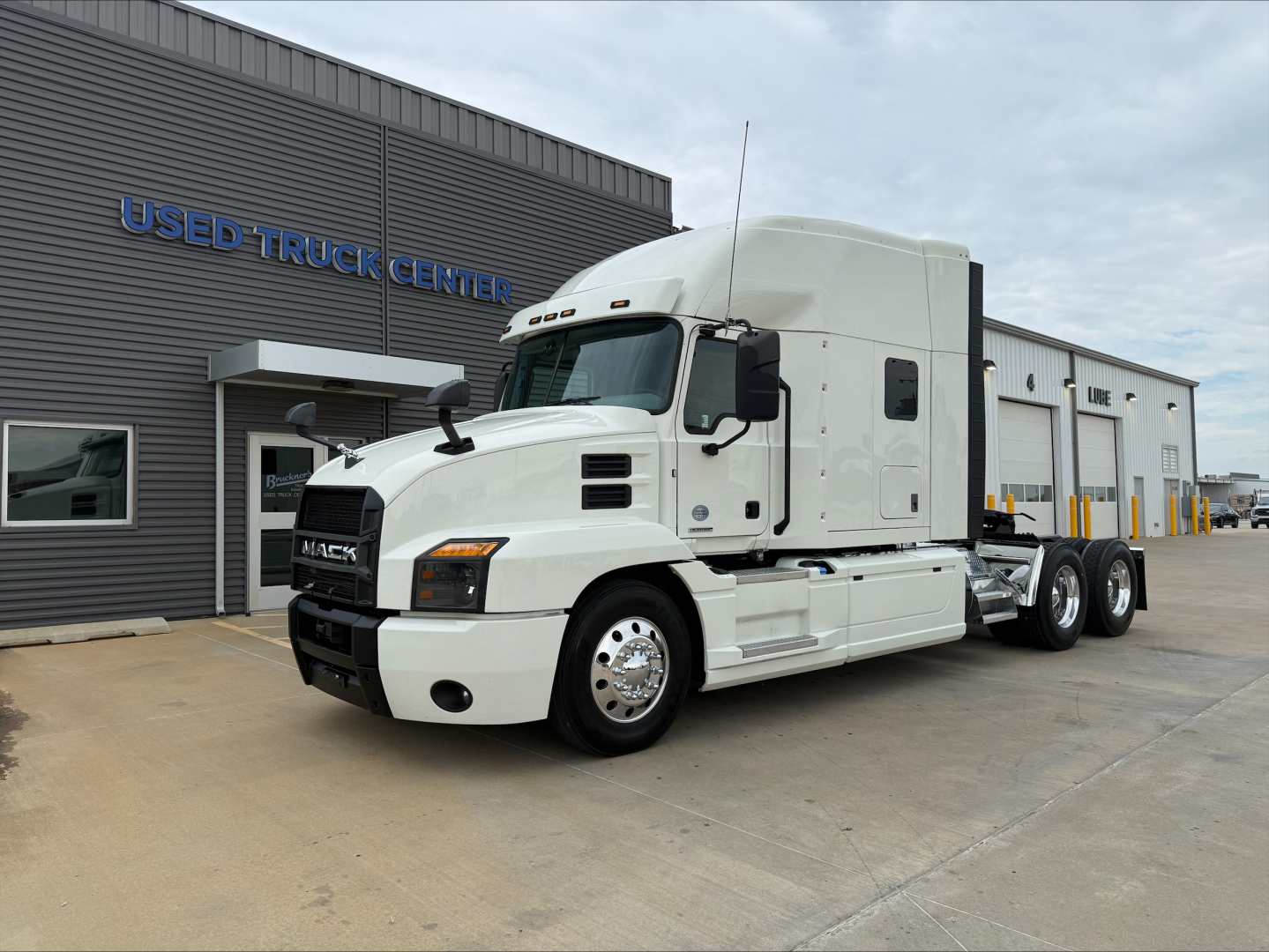 White 2020 Mack Anthem conventional sleeper truck in front of a used truck center building.