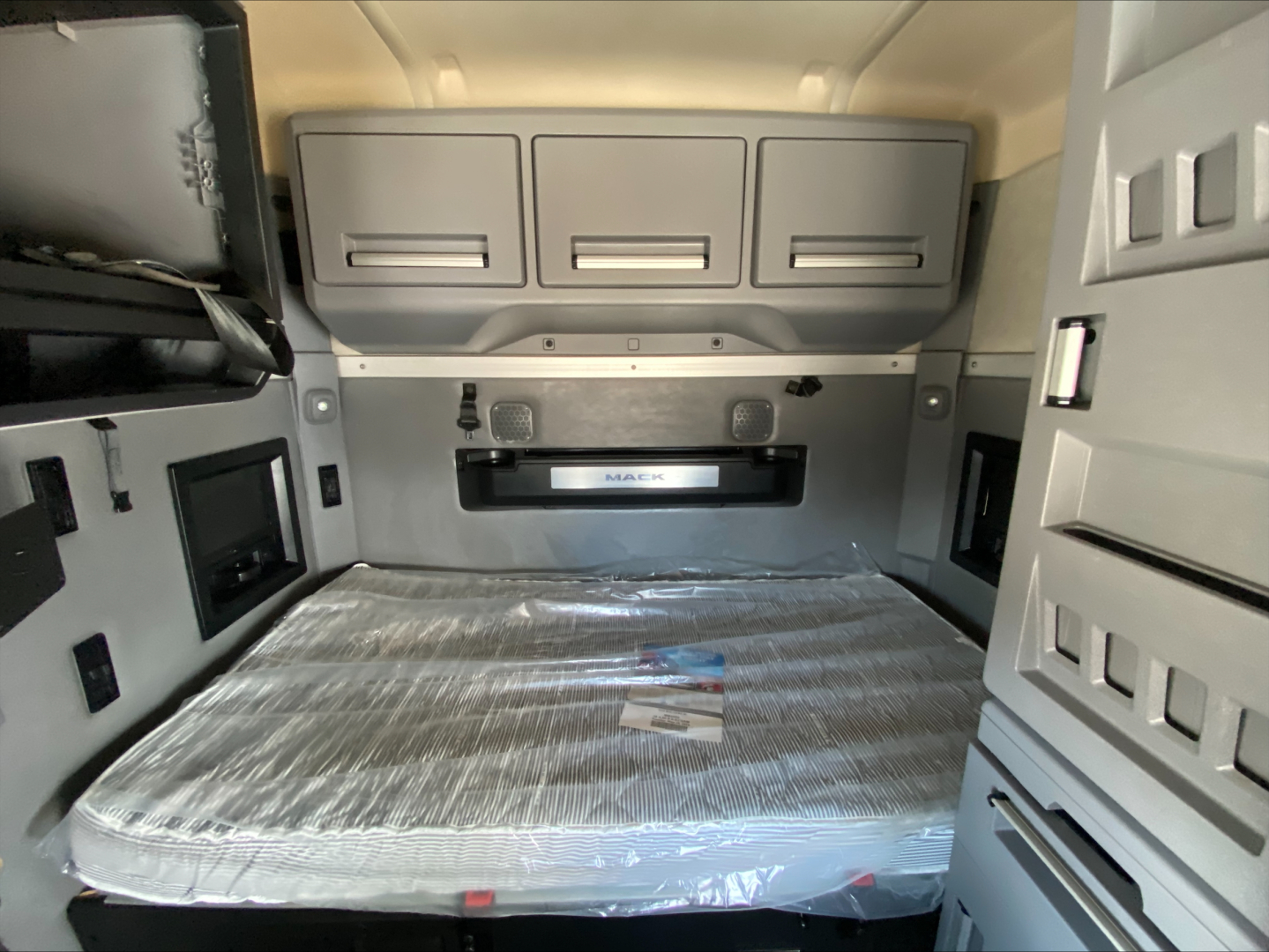 Truck cab interior showing sleeper area with overhead storage cabinets and a wrapped mattress.