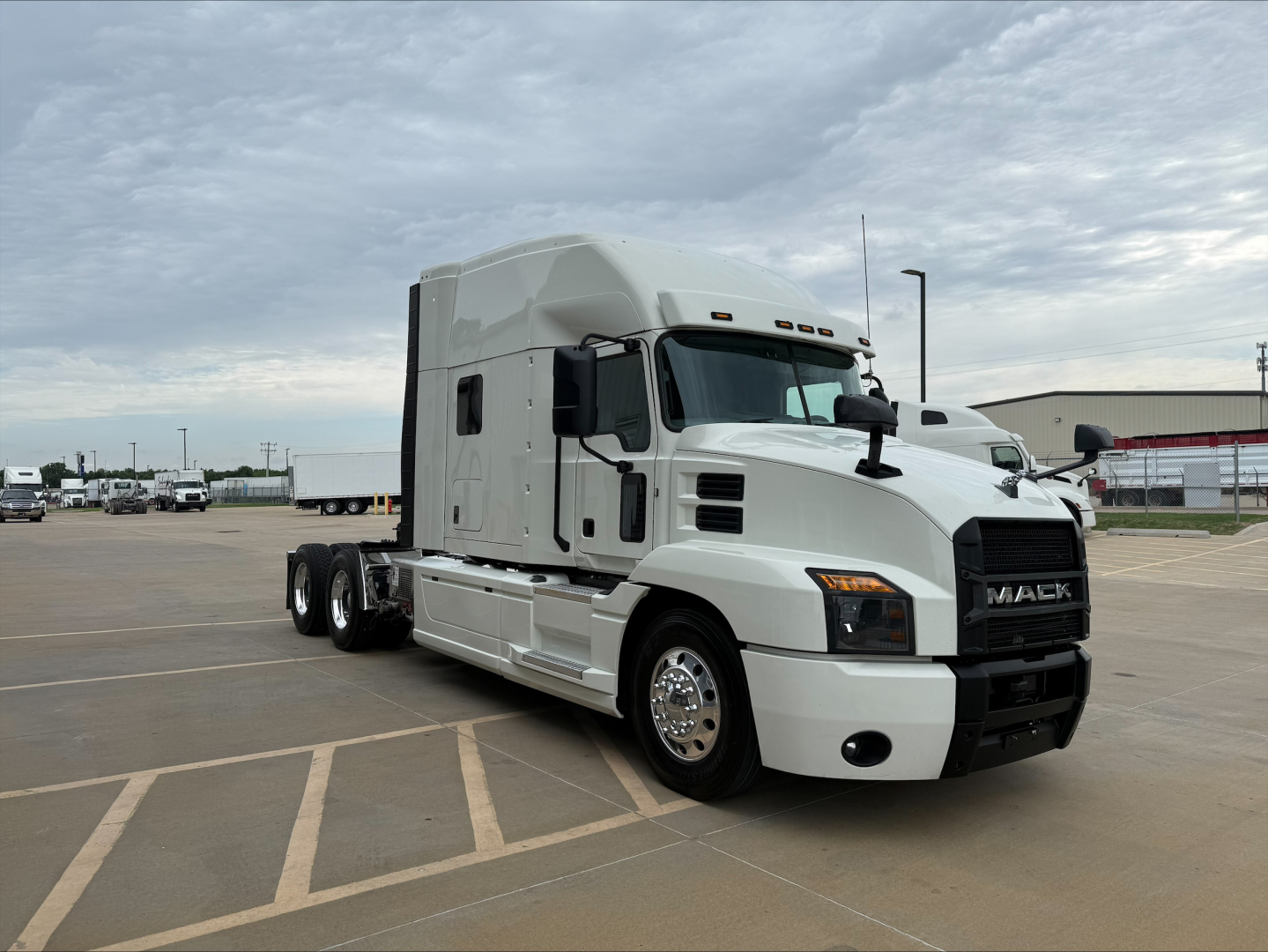Truck side view of a white 2020 Mack Anthem conventional sleeper with dual rear axles and Mack grille, parked in lot.
