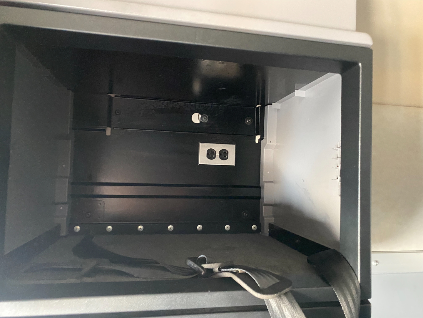 Open storage compartment in a truck showing shelves and a small metal plate with two screws and a white label. No other text readable.