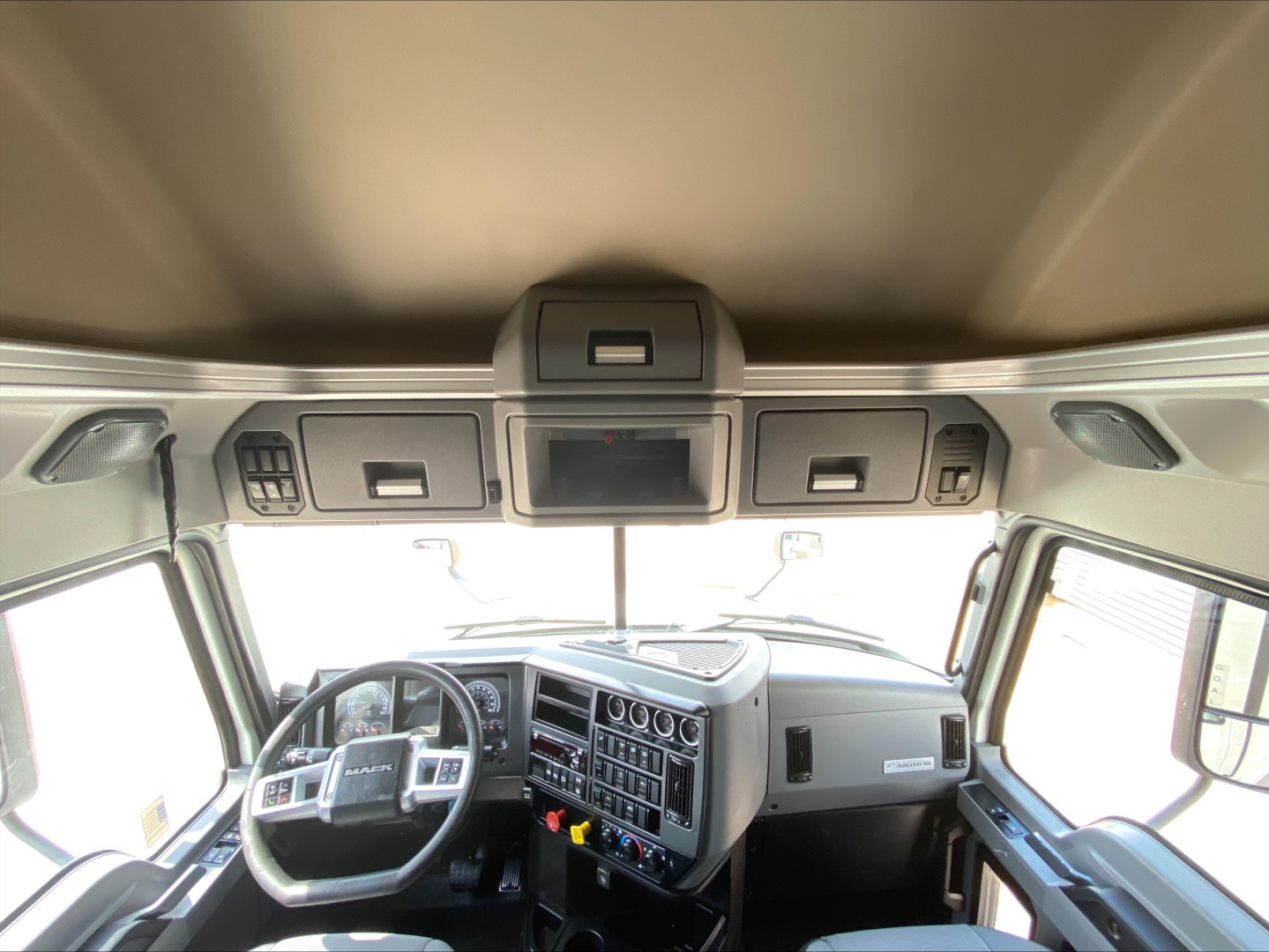 Truck cabin interior of a 2020 Mack Anthem showing steering wheel, instrument cluster, center console, and overhead storage panels.