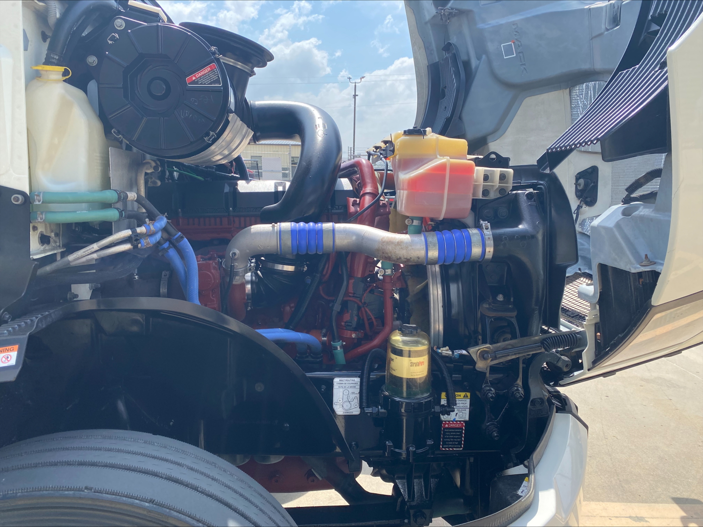 Engine bay of a 2020 Mack Anthem showing coolant reservoir, yellow dipstick, hoses, and various metal components.