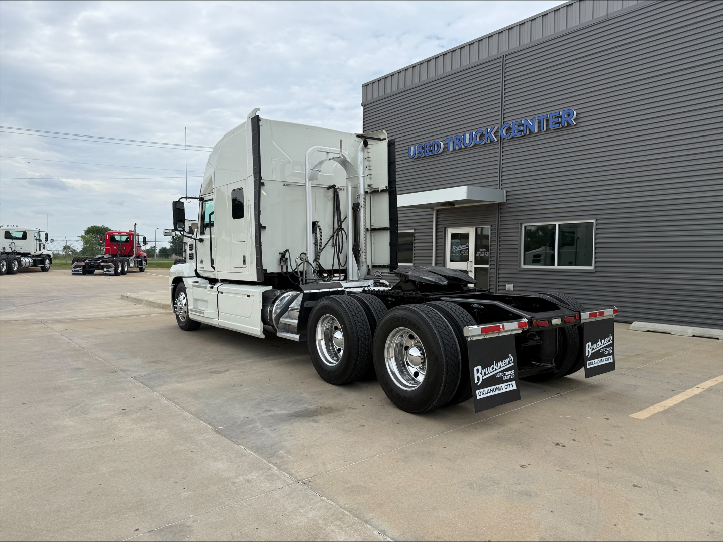 Truck tractor tractor rear view showing fifth wheel, dual rear axles, and dealership building in background with 'TRUCK CENTER' sign.