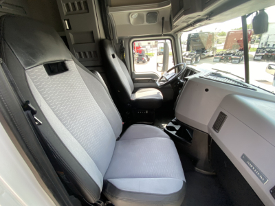 Truck cab interior of a 2020 Mack Anthem showing the driver seat and passenger seat with light gray upholstery, dashboard, and steering wheel visible.