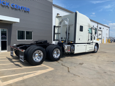 Truck chassis and cab of a 2020 Mack Anthem Conventional Sleeper, side view, with dual rear axles and fuel tanks visible, dealership lot in background