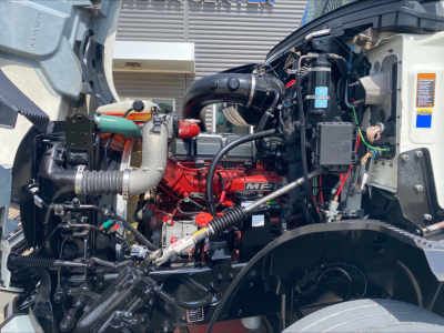 Truck engine bay of a 2020 Mack Anthem with red engine, black hoses, and various components visible in the foreground.