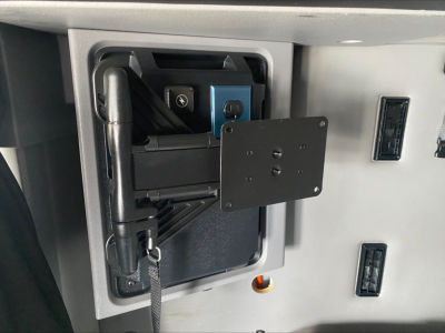 Truck interior showing a mounted equipment bracket with a blue device inside a recessed compartment.