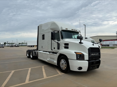 Truck side view of a white 2020 Mack Anthem conventional sleeper with dual rear axles and Mack grille, parked in lot.