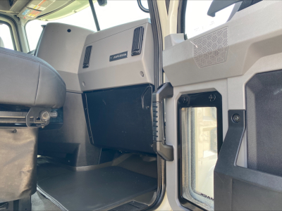 Truck cab interior showing Mack ANTHEM badge on dash panel and open door with window; visible glovebox and trim panels in the cab.
