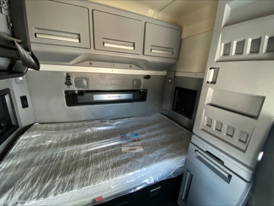 Truck sleeper cab interior with overhead cabinets and a bed; visible text includes a Mack dashboard area and a mattress still wrapped.