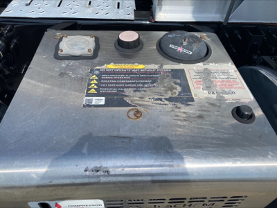 Gauge-free view of Mack ANTHEM fuel/auxiliary tank cap area with warnings label and two caps; metal surface shows sticker warnings and circular cap near center.