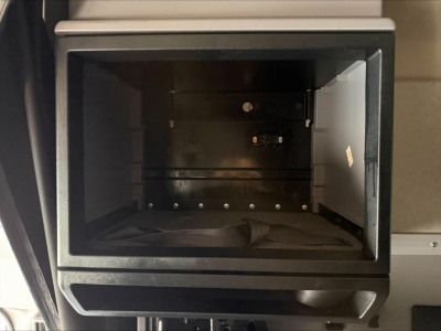 Cabinet-style storage compartment open with an empty interior and a dark, metallic surface; small screws visible along the bottom edge.