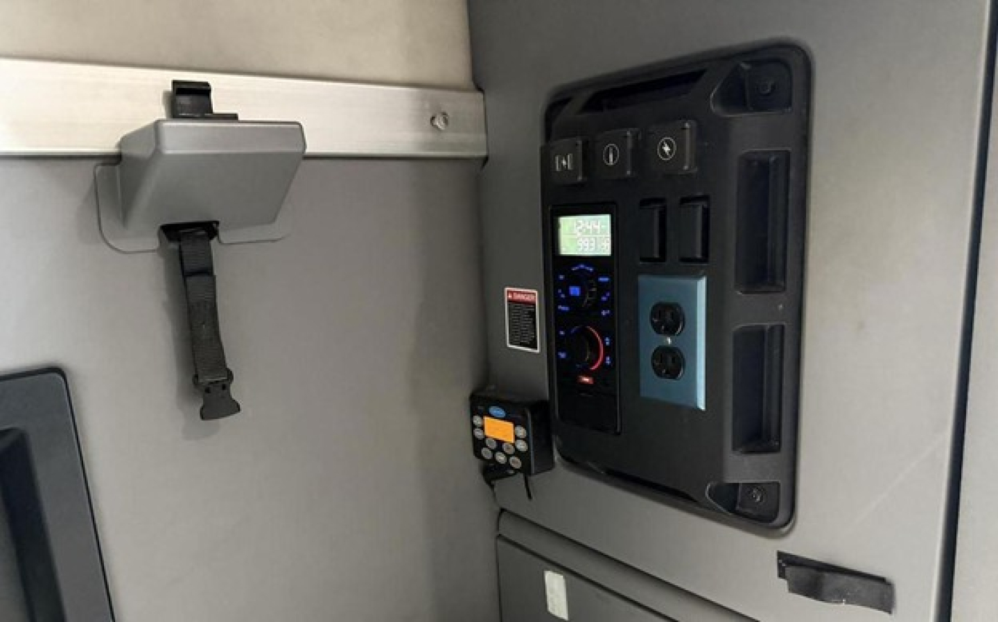 Truck cab interior panel with control unit and digital display, electrical outlets, and control switches inside a Mack Anthem sleeper cab.