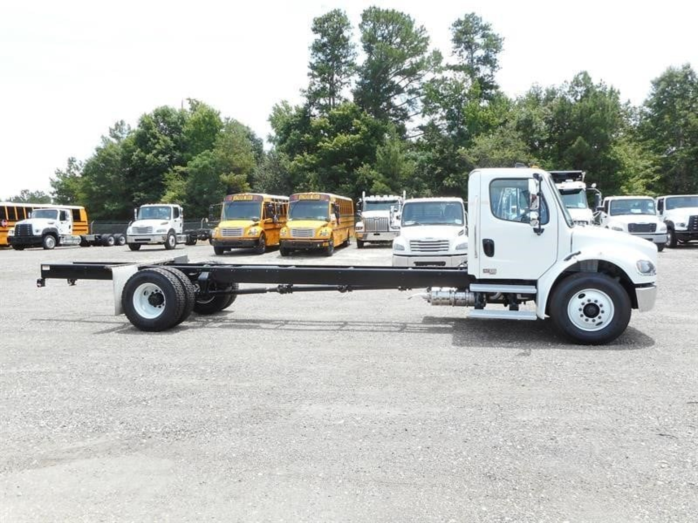 Freightliner M2 106 cab and chassis truck in a listing photo showing a white front cab with long chassis frame and single rear axle, lot of vehicles in background