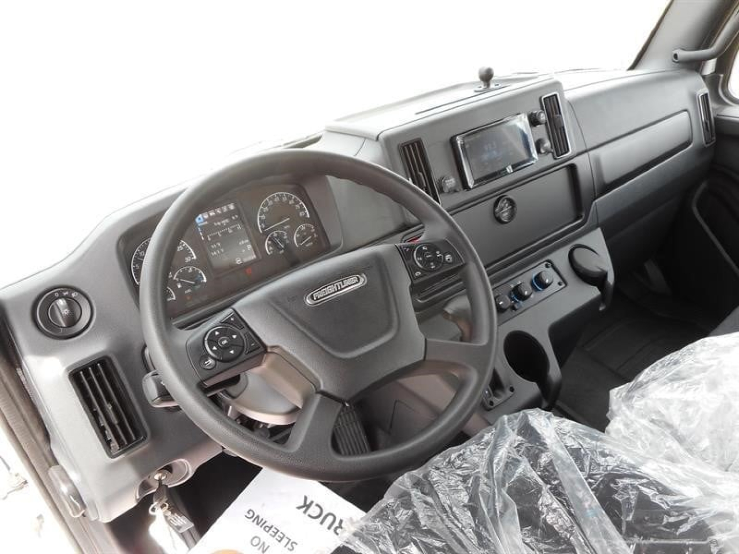 Cab interior of a Freightliner M2 106 truck showing steering wheel, dashboard, and center console with digital display.