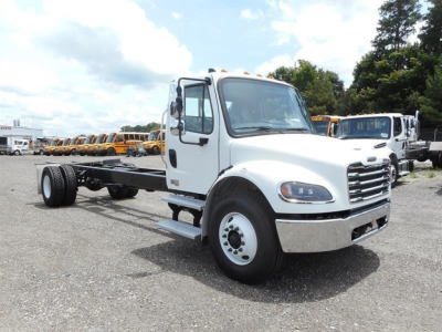 Freightliner M2 106 cab chassis in white, front three-quarter view, with chassis and rear axle exposed, dealership lot in background.