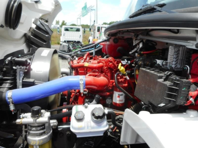 Freightliner M2 106 engine bay showing red engine components, blue hose, and various fluid reservoirs and wiring harnesses.