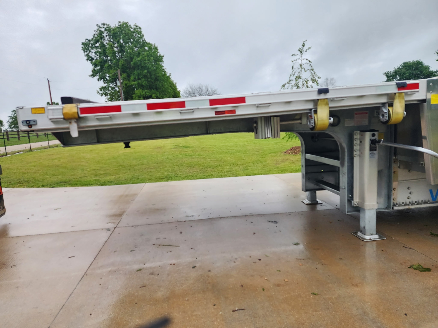 Trailer with drop deck showing structural frame and support legs, side rails and reflective tape along top edge.
