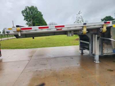 Trailer with drop deck showing structural frame and support legs, side rails and reflective tape along top edge.