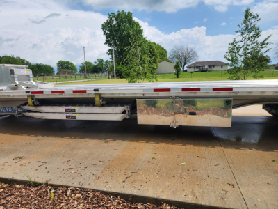 Trailer side view showing reflective aluminum toolbox and lower deck with polished steel panels and safety rails.
