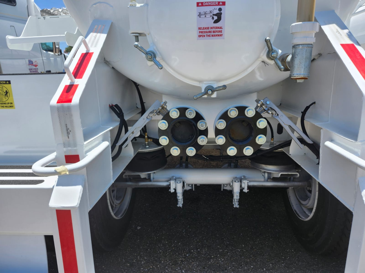 Rear view of vacuum tanker trailer showing twin hose connections and central mounting assembly with circular ports and warning label.