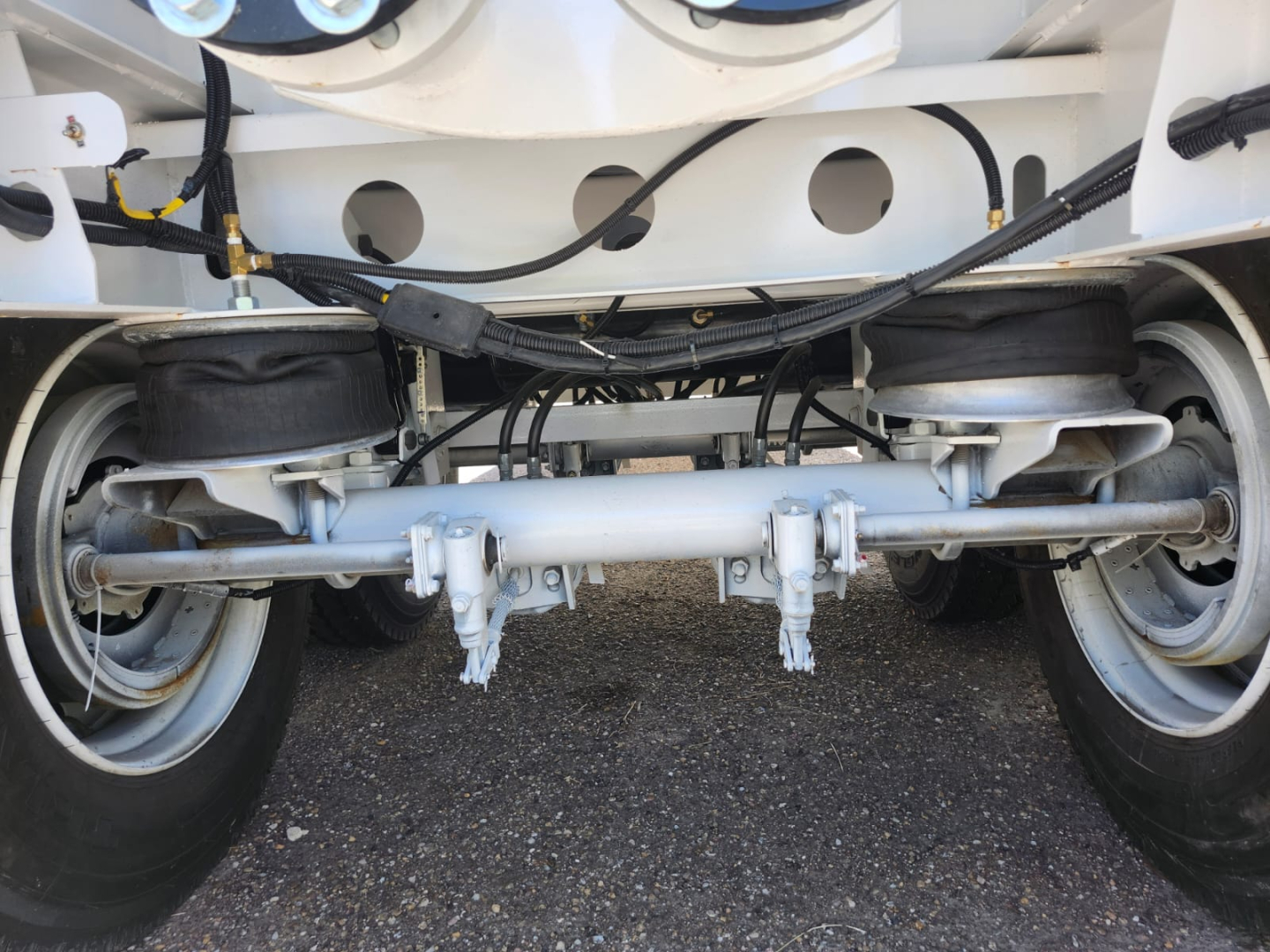 Trailer suspension and aboveperson showing air spring bags, axle beam, and dual wheels under vacuum tank trailer.