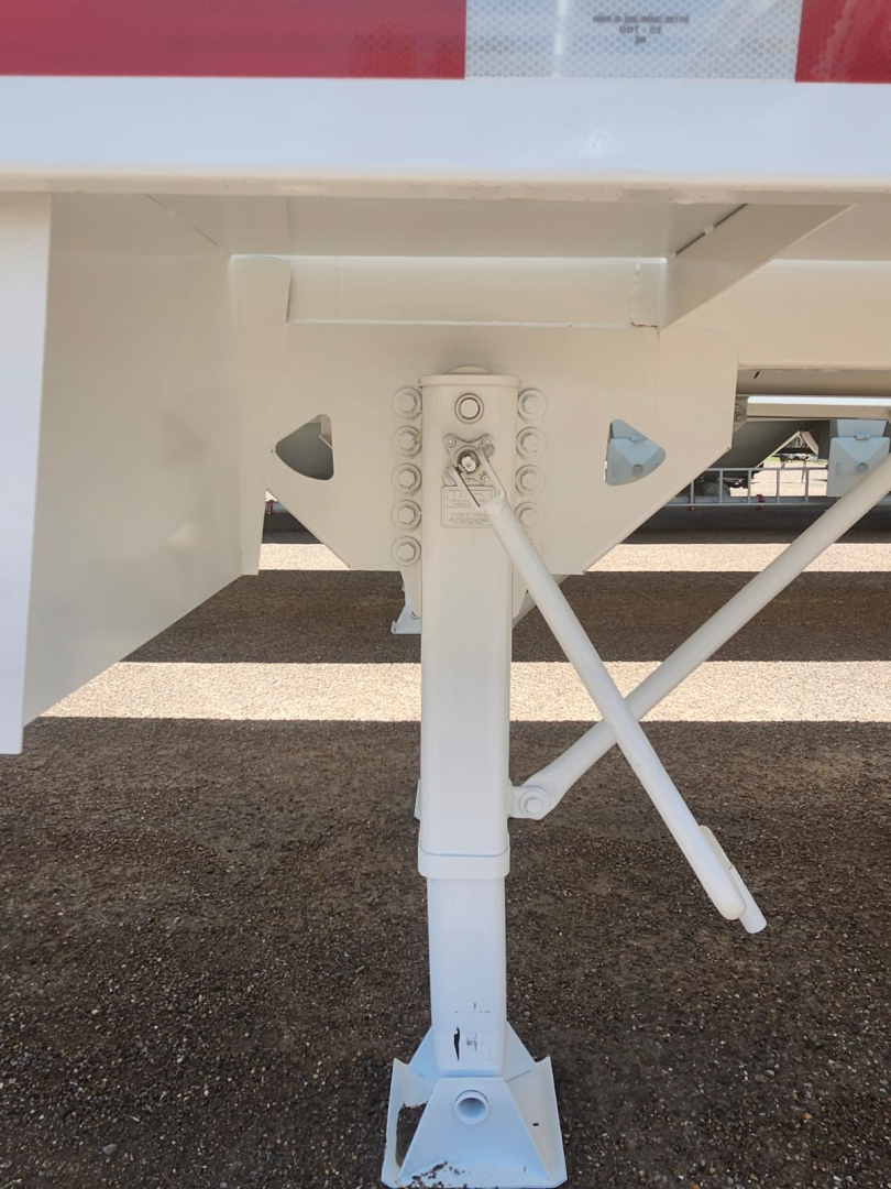 Trailer landing gear and support frame of a vacuum tank trailer with white paint and stabilizer legs visible.