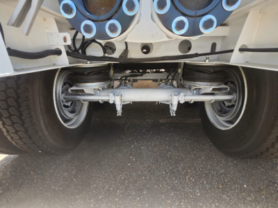 Trailer underside showing vacuum steel tank with dual rear axles and suspension beam in view.