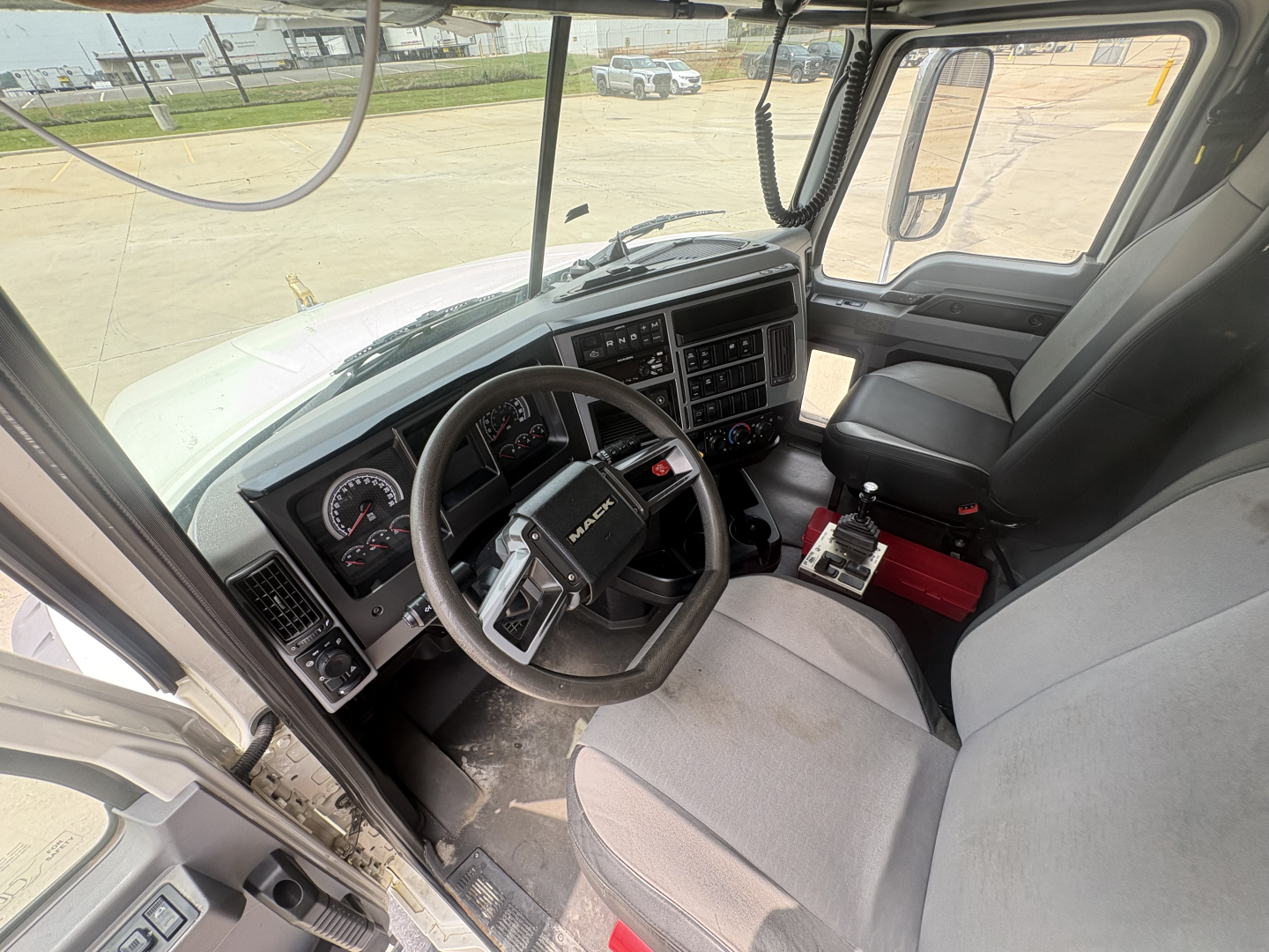 Truck cab interior showing steering wheel, dashboard, and driver seat of a 2020 Mack GR64F. Text visible on dashboard panels and controls but not legible in detail.