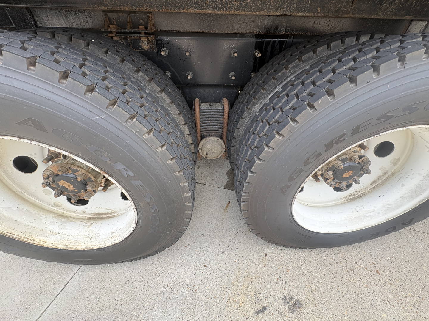 Dual rear wheels showing tire treads and the drop axle center with leaf spring in between, part of a Mack GR64F truck chassis.