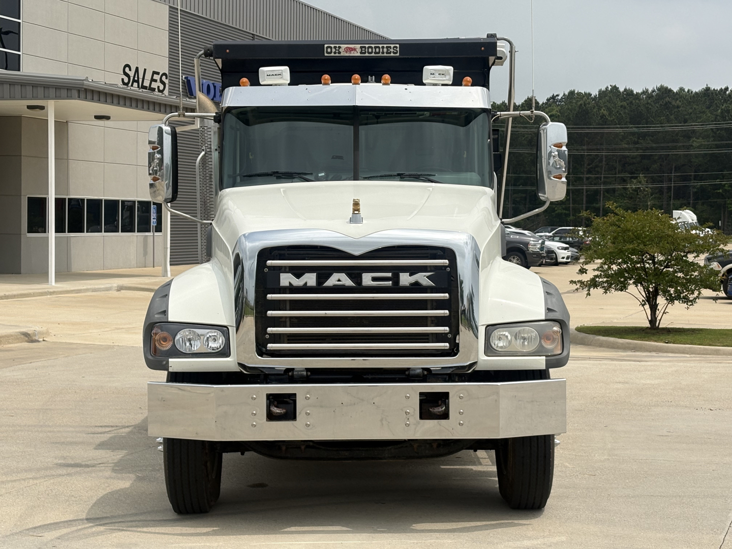 Mack GR64F front view showing chrome grille with MACk emblem and large bumper, white cab, dump truck, VIN plate area not visible.