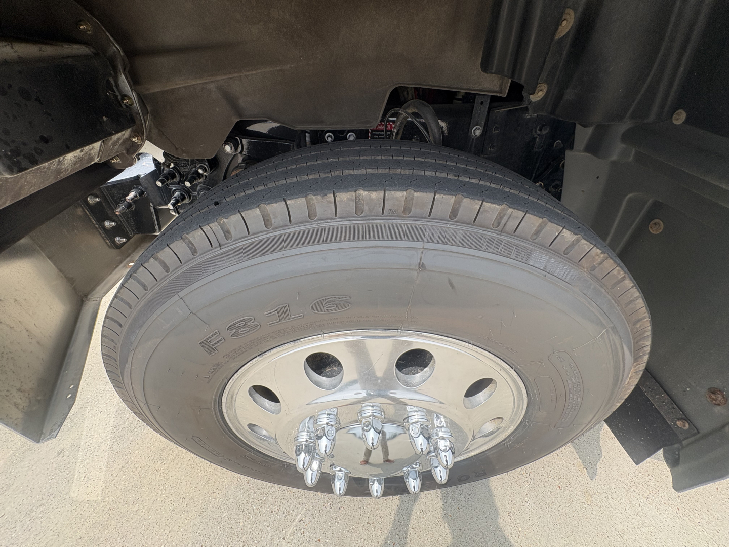 Wheel and tire close-up on a Mack GR64F dump truck showing front axle hub with lug nuts and part of the wheel well.