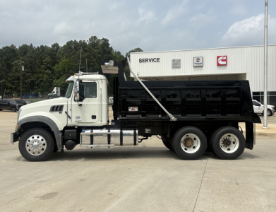 Truck side view showing a white 2020 Mack GR64F dump truck with black dump body and dual rear axles in front of a service building.