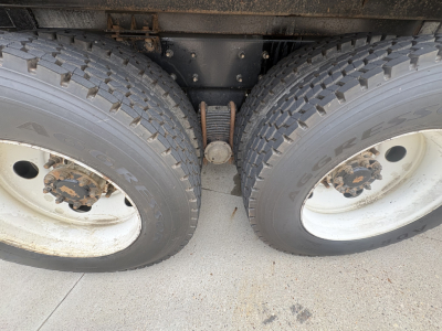 Dual rear wheels showing tire treads and the drop axle center with leaf spring in between, part of a Mack GR64F truck chassis.