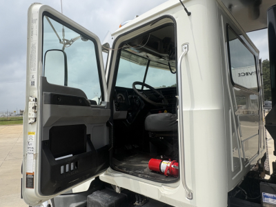 Cab opening of a 2020 Mack GR64F dump truck showing open driver door with interior dash and steering wheel visible; fire extinguisher on floor, light gray interior panels.